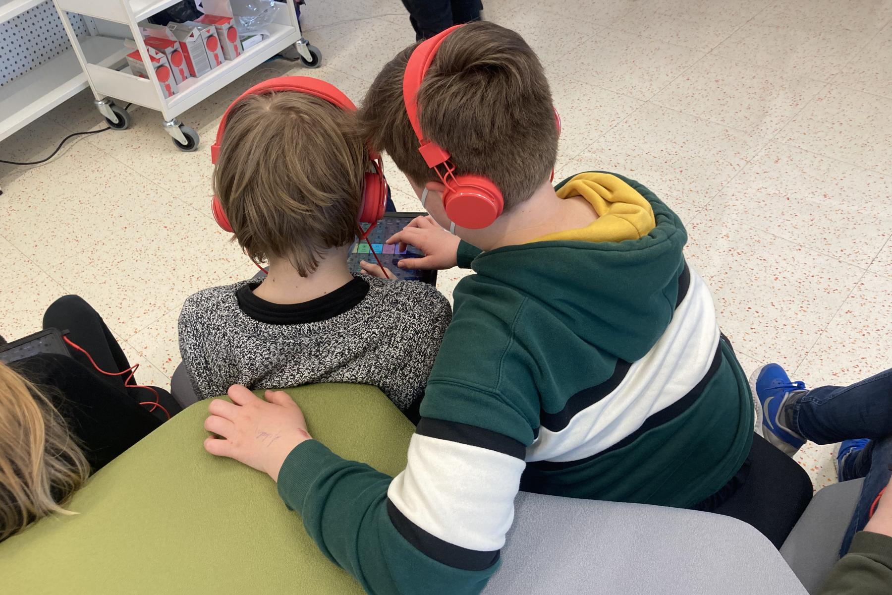 Zwei Jungs sind von hinten zu sehen. Sie sitzen ind er Bibliothek udn tragen Kopfhörer