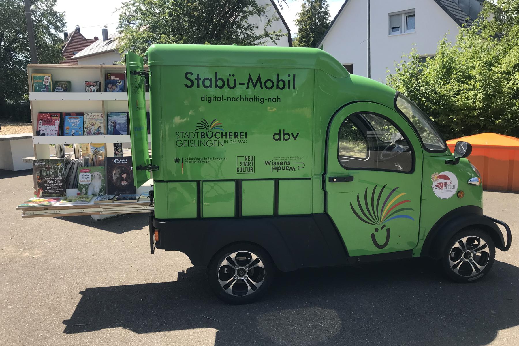Grünes Stabü-Mobil mit geöffnetem Heck, aus dem eine Bücheregal herausragt.