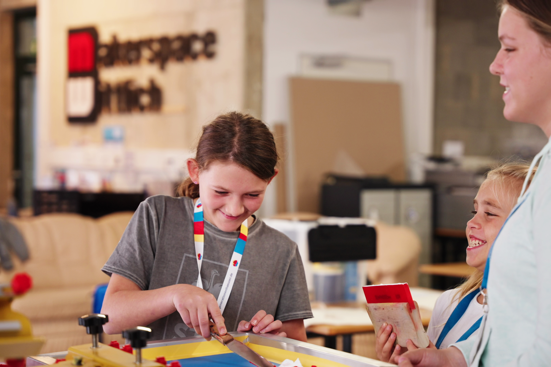 Zwei Schülerinnen sind im Makerspace der Stadtbücherei Wittlich beim werkeln zu sehen. Sie lachen. Mit dabei ein ältrere Person.