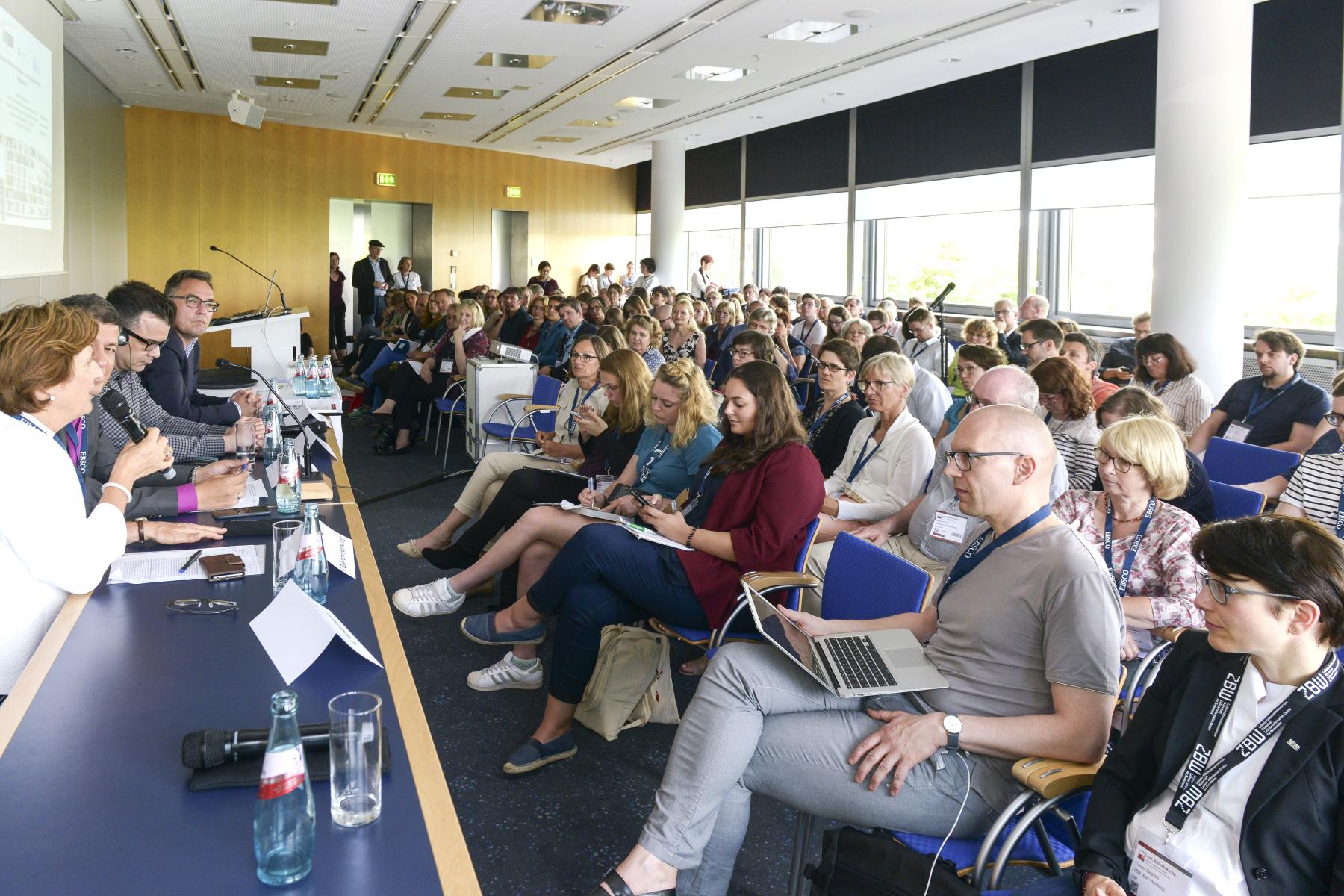 Eine Podiumsdiskussion in Messeräumen mit vier Diskutantinnen und der Raum ist voll mit Zuhörerinnen.
