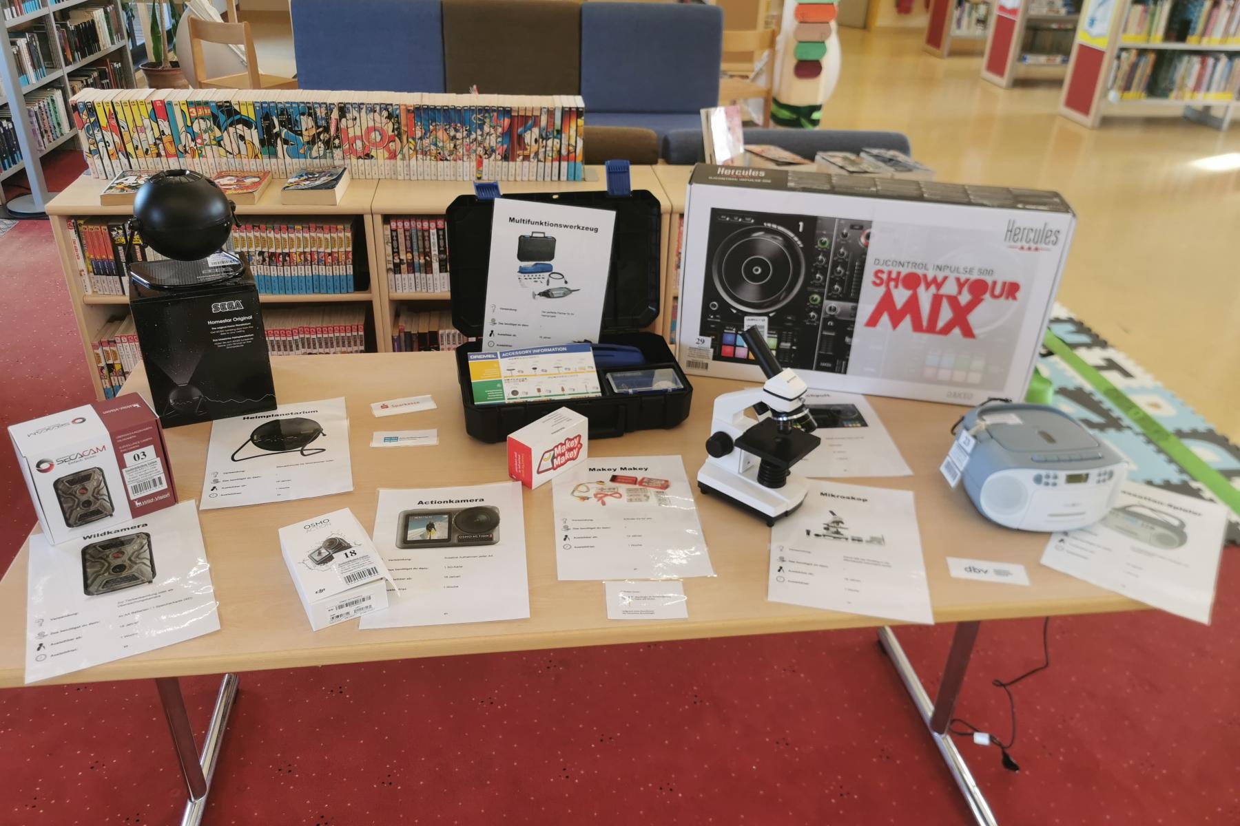 Tisch mit ausleihbaren Dingen, wie einen Mikroskop oder einen CD-Player in der Stadtbibliothek Guben. 