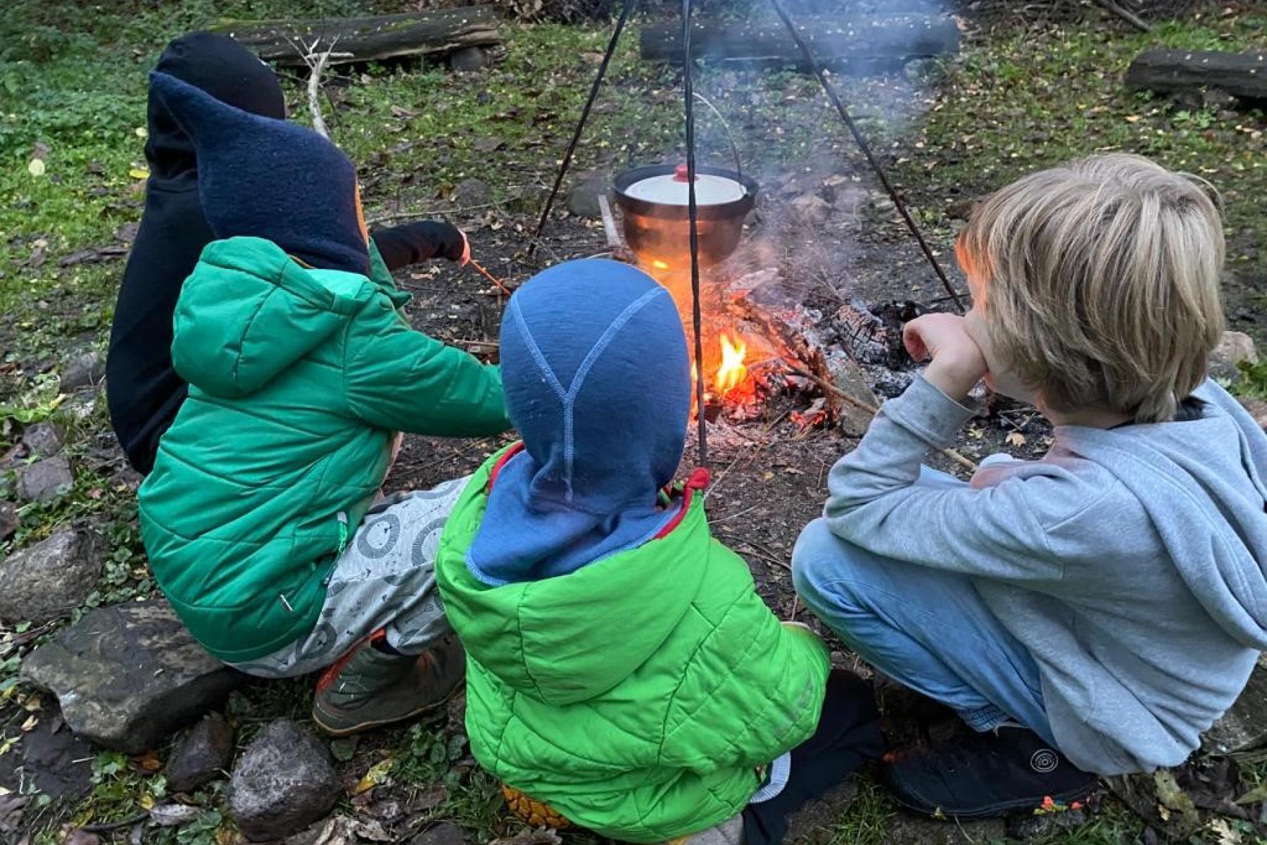 Kinder sitzen um eine Schale über einem Lagerfeuer.