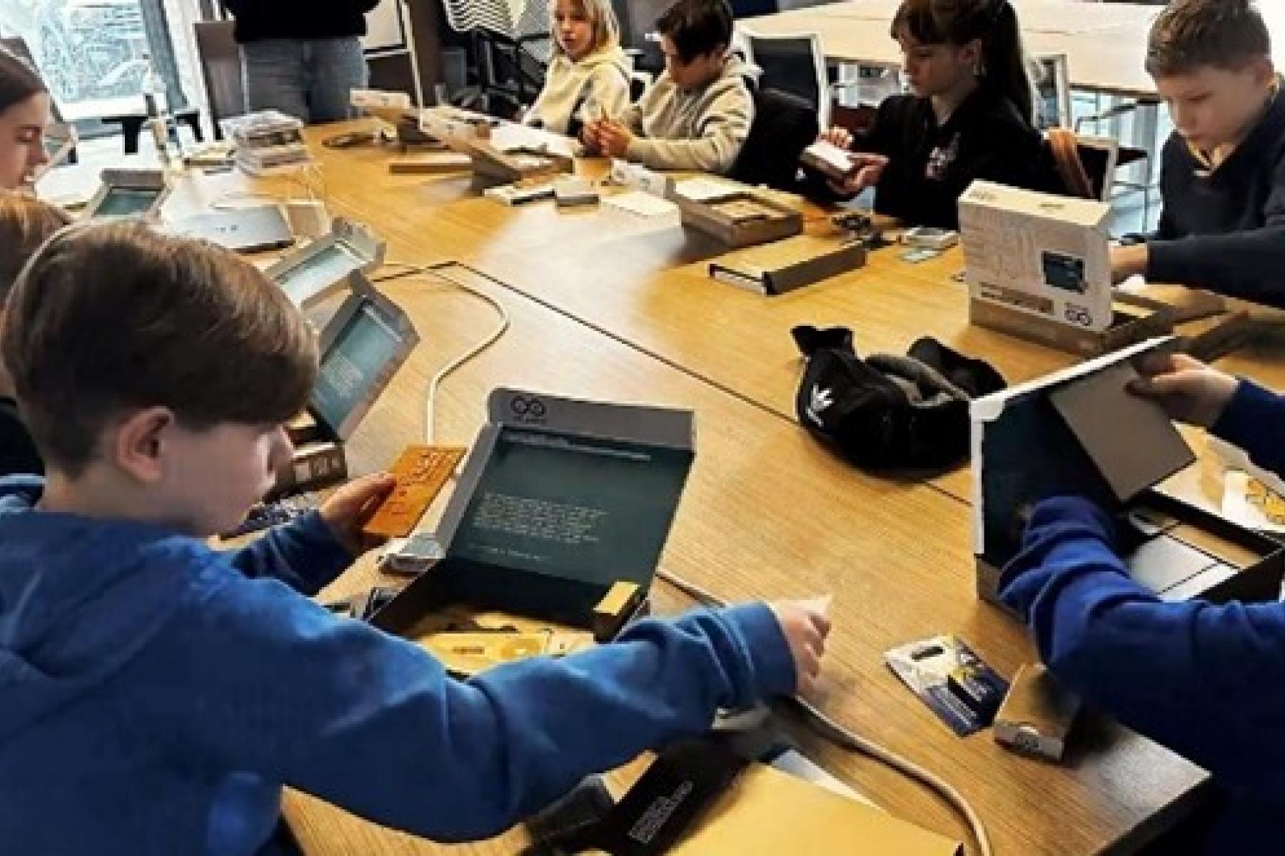 Kinder sitzen mit digitalen Geräten um einen Tisch
