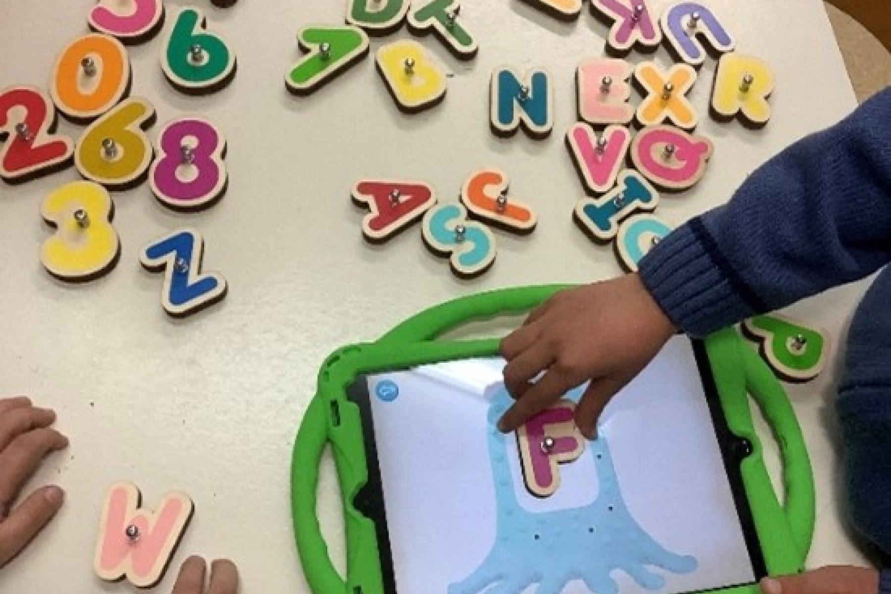Ein Kind legt einen Holzbuchstaben auf ein Tablet