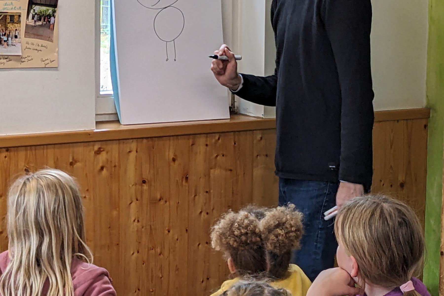 Ein Mann zeichnet etwas auf Papier mit einer Gruppe Kindern, die zuschaut.