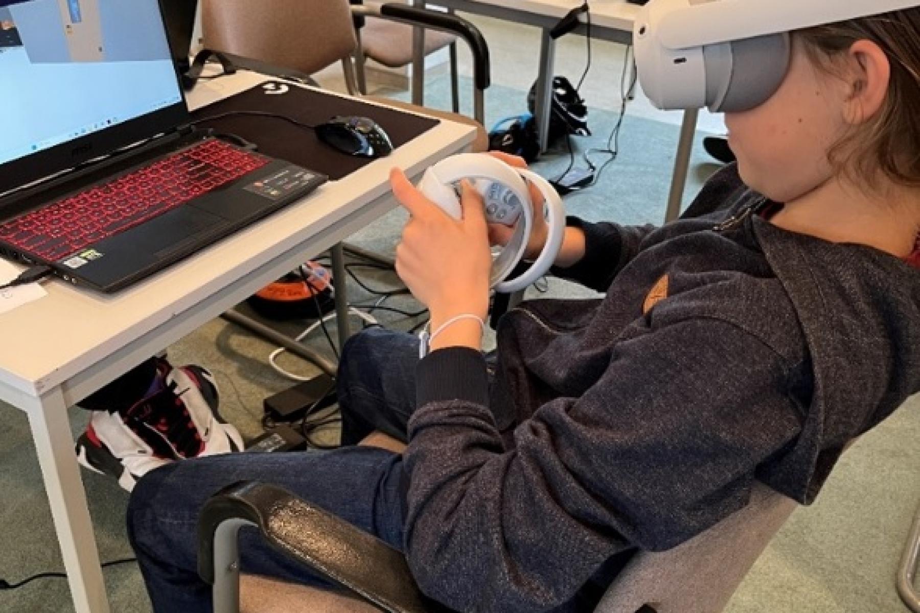 Kind sitzt mit VR-Brille vor einem Laptop.