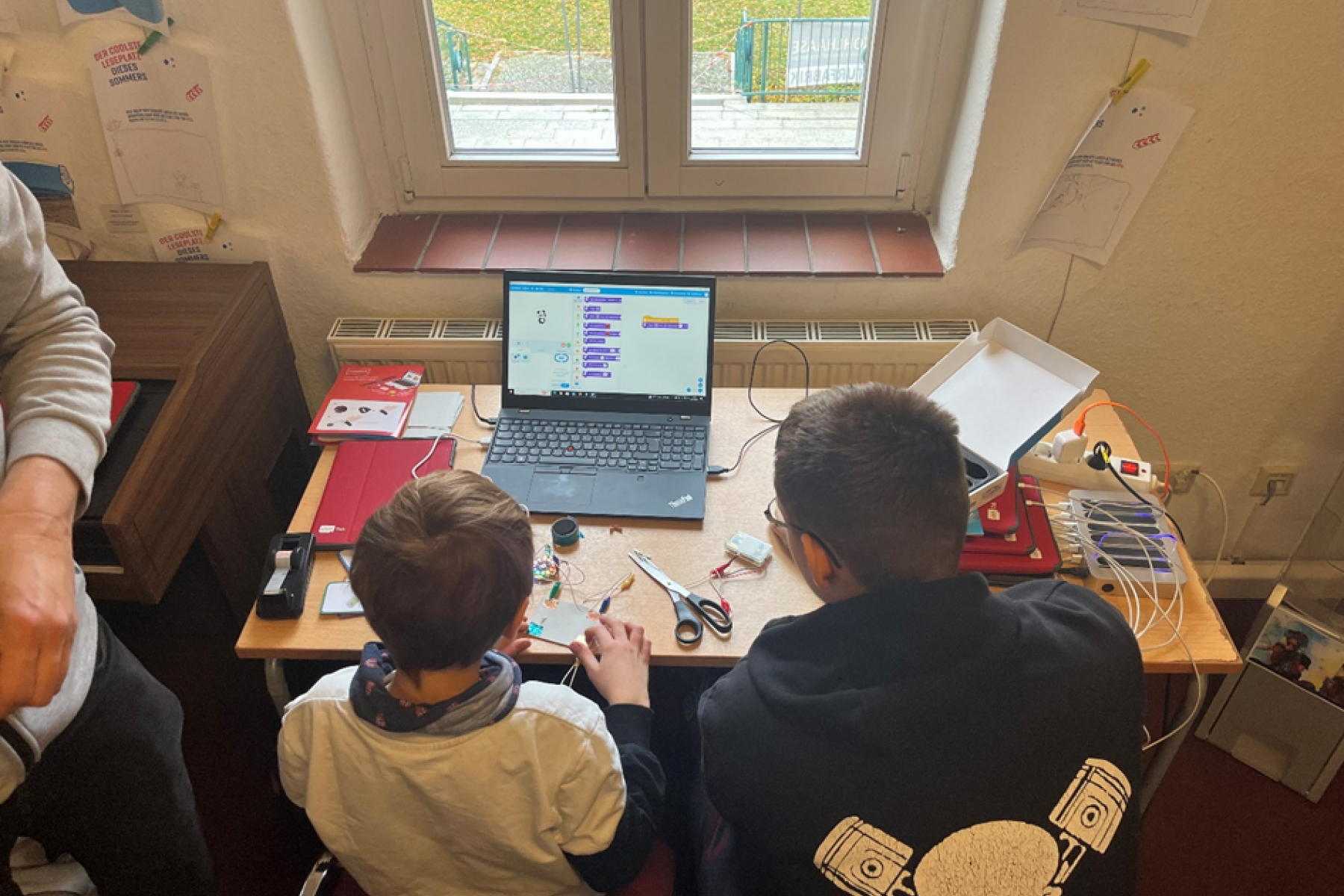 Zwei Jungs sitzen am Computer und programmieren einen Roboter.