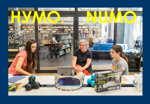 Foto mit drei Personen, die in einer Bibliothek sitzen und gemeinsam auf einen Laptop schauen. Oben auf dem Foto steht Text in gelber Schrift: НУМО. NUMO.