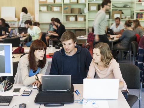 Drei Studenten sitzen zusammen und schauen in einen Laptop