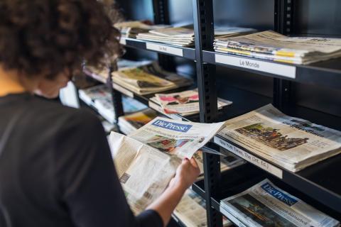 Frau steht an Presseregal in der bibliothek und liest Zeitung