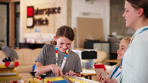 Zwei Schülerinnen sind im Makerspace der Stadtbücherei Wittlich beim werkeln zu sehen. Sie lachen. Mit dabei ein ältrere Person.