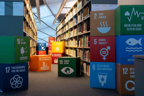 Bucherregalgang und drumherum bunte Kartons mit SDGs.