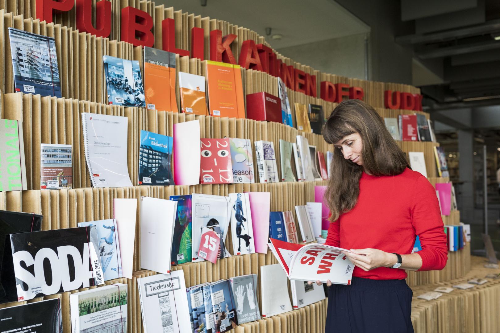 Frau in rotem Pullover vor einem geschwungenen Bücherregal.