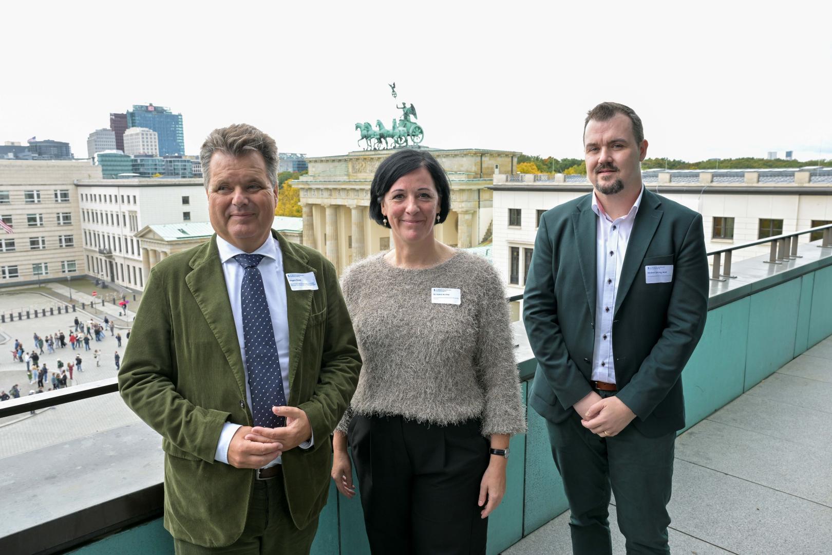 Drei Personen stehten auf einem Balkon und lächeln in die Kamera.