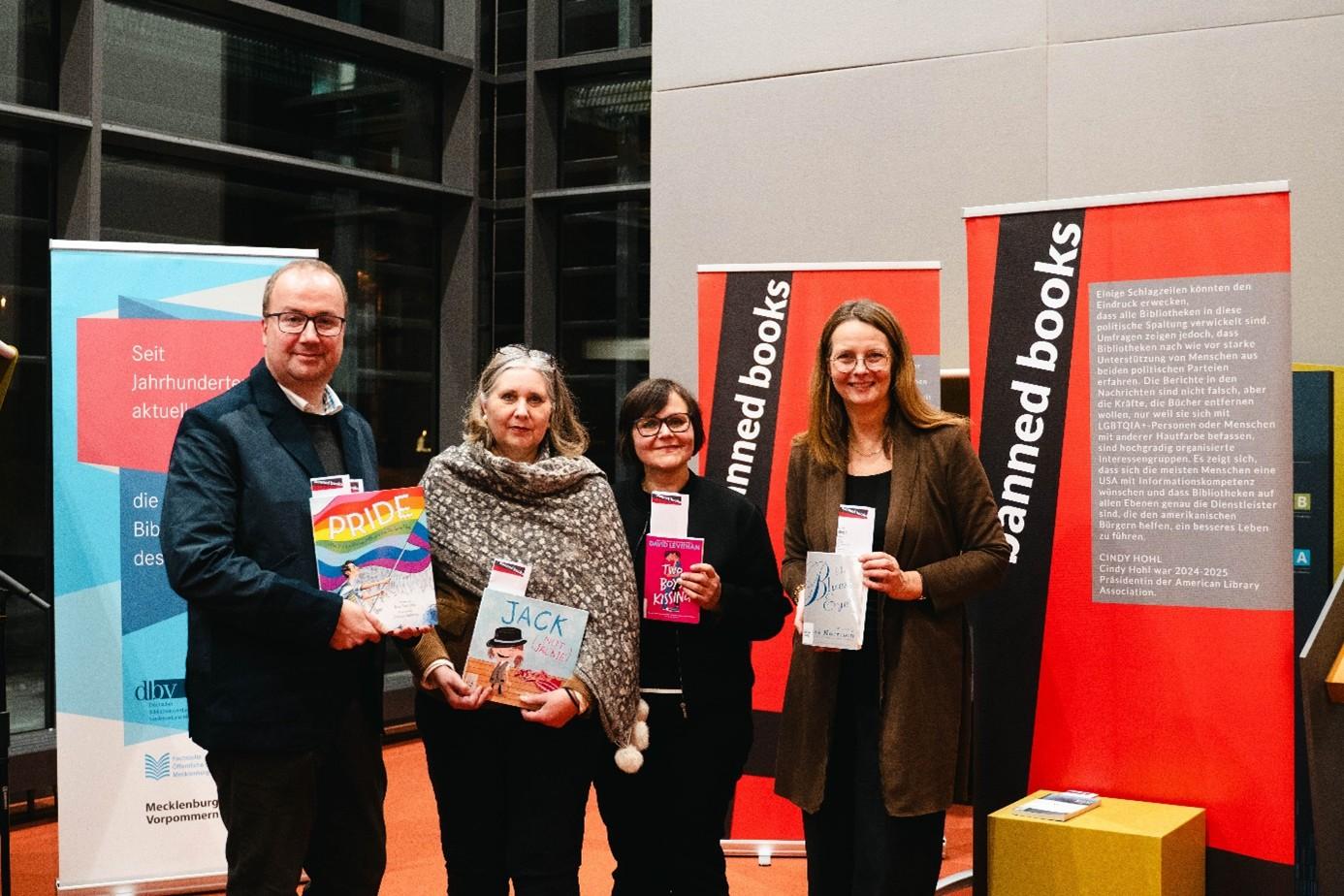 Vier Personen mit Büchern vor Roll-ups