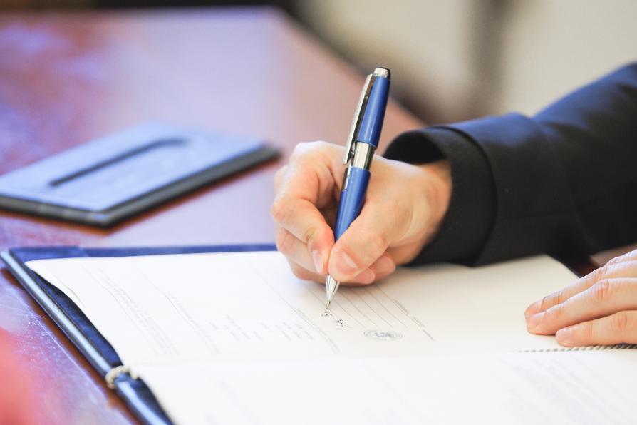 Hand mit Stift unterschreibt Urkunde