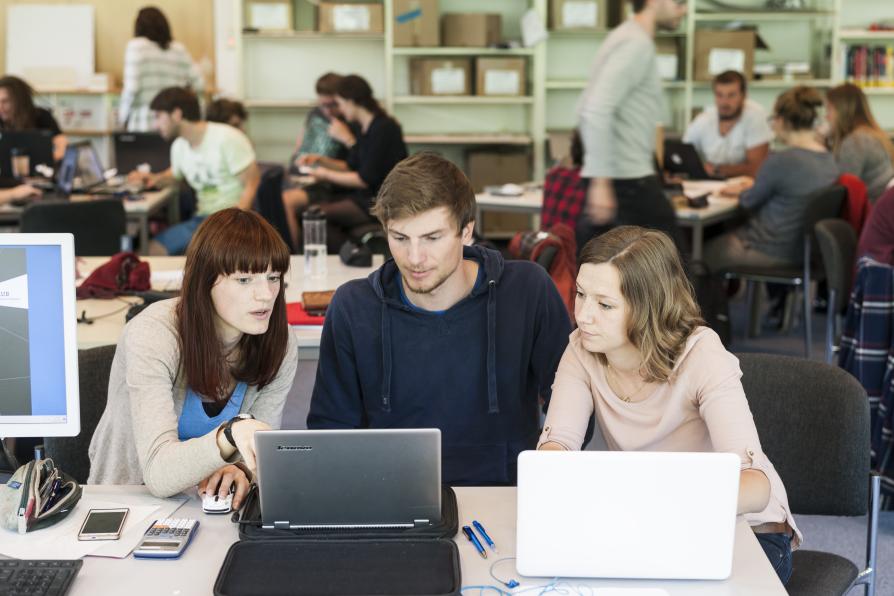 Drei Studenten sitzen zusammen und schauen in einen Laptop