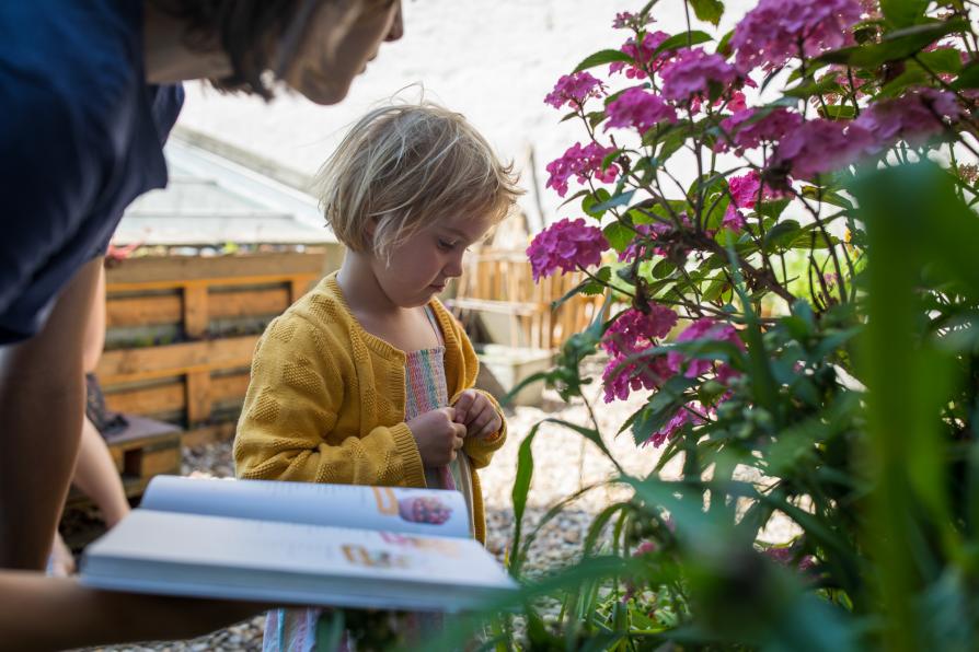 Kind und Frau stehen an eine Pflanze udn schauen sich ein Buch an