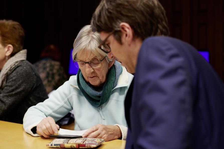 Seniorin und ein Herr mittleren Alters sitzen zusammen am Tisch und schauen auf ihr Handy