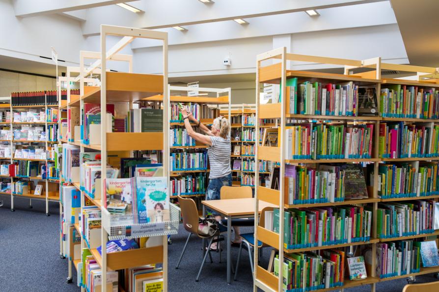 Bücherregale in der Bibliothek. Eine Frau sucht in einem der Regale.