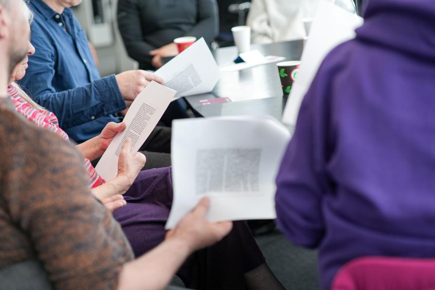 Gruppe mit Textauszügen in den Händen sitzt gemeinsam am Tisch