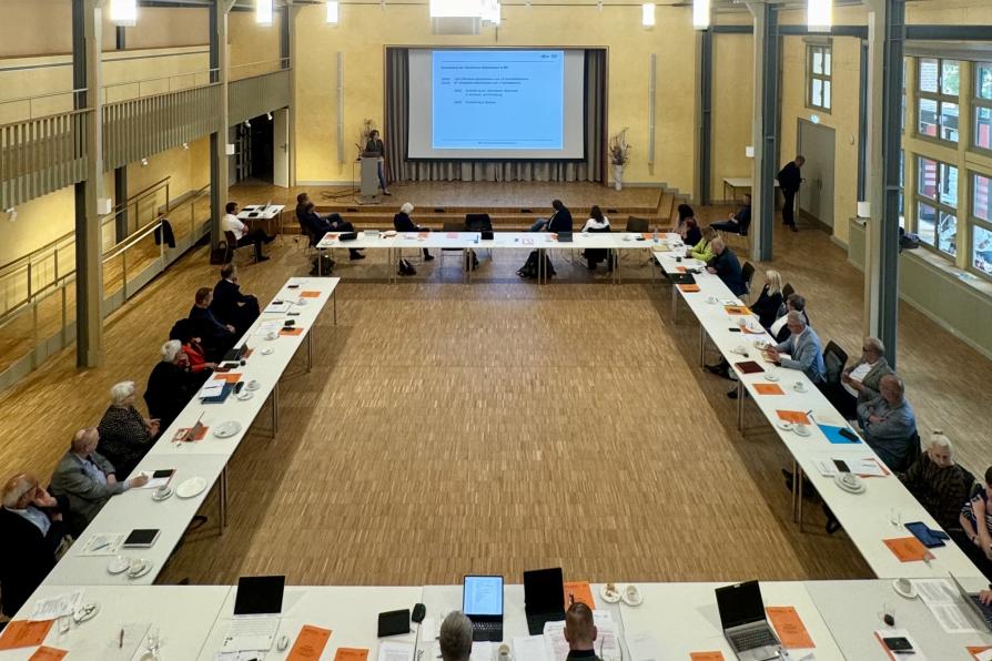 Sitzungsaal, die Teilnehmerinnen sitzen an Tischen, vorne eine Präsentation