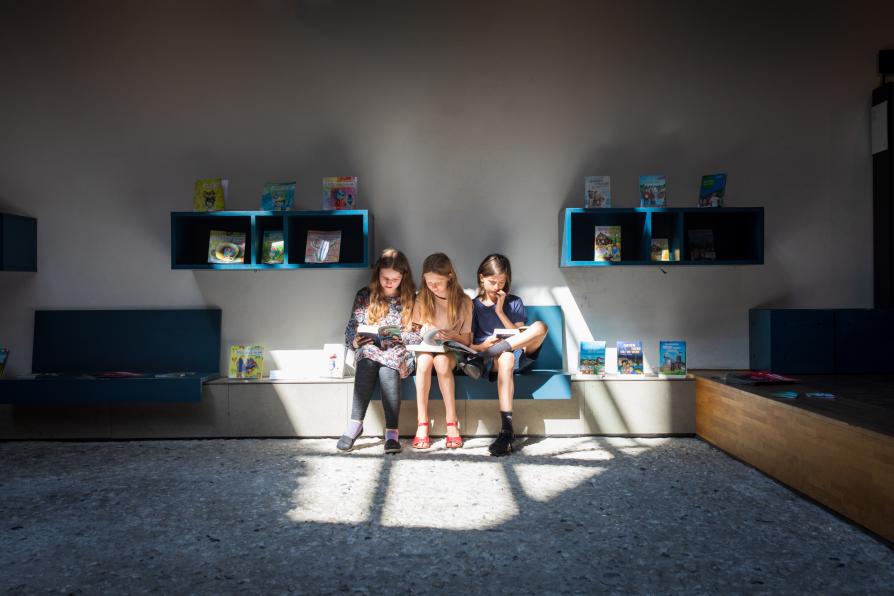 Drei Schüler*innen sitzen in der Bibliothek und Lesen. Sie werden von einem Lichtkegel angeleuchtet.