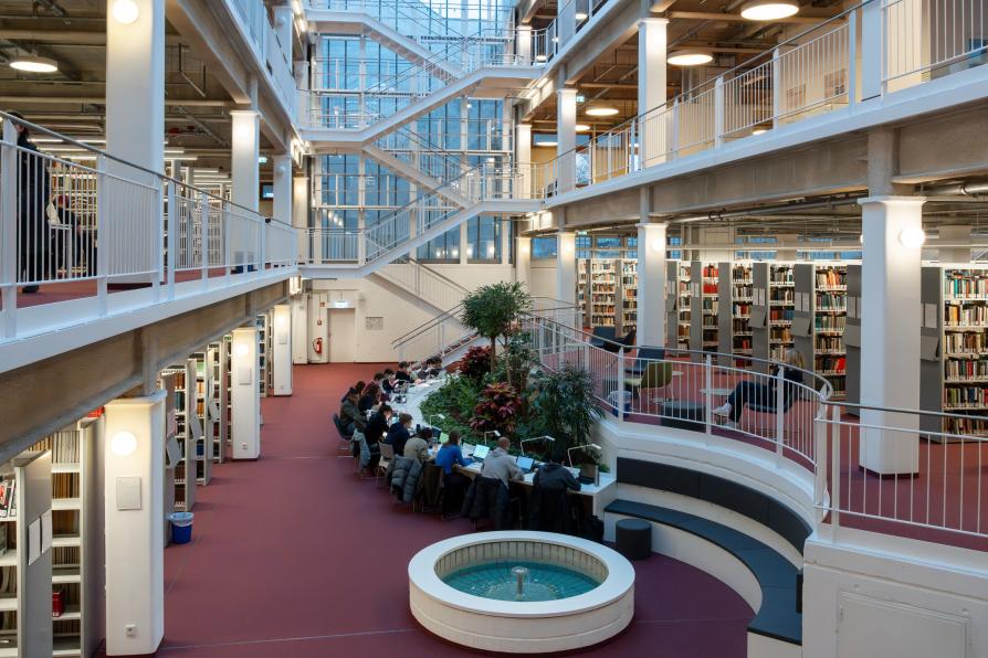 Innenraum einer Unibibliothek, lernende Studentinnen an im Halbkreis aufgestellten Tischen