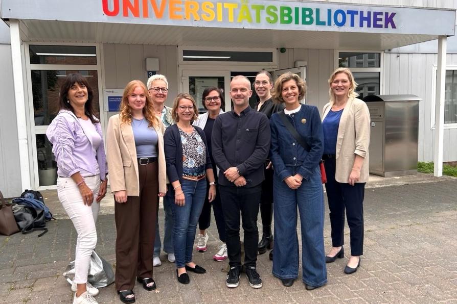 Neun Personen stehen vor dem Eingang der Universitätsbibliothek