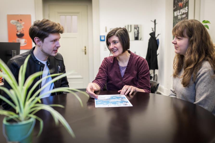 Drei Personen sitzen um einen Tisch und sind im Gespräch