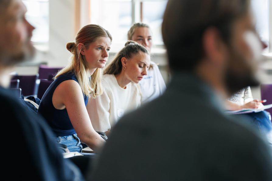 Es sitzen mehrere Personen in einer Workshopsituatuon, der Fokus ist auf eine Frau gerichtet.