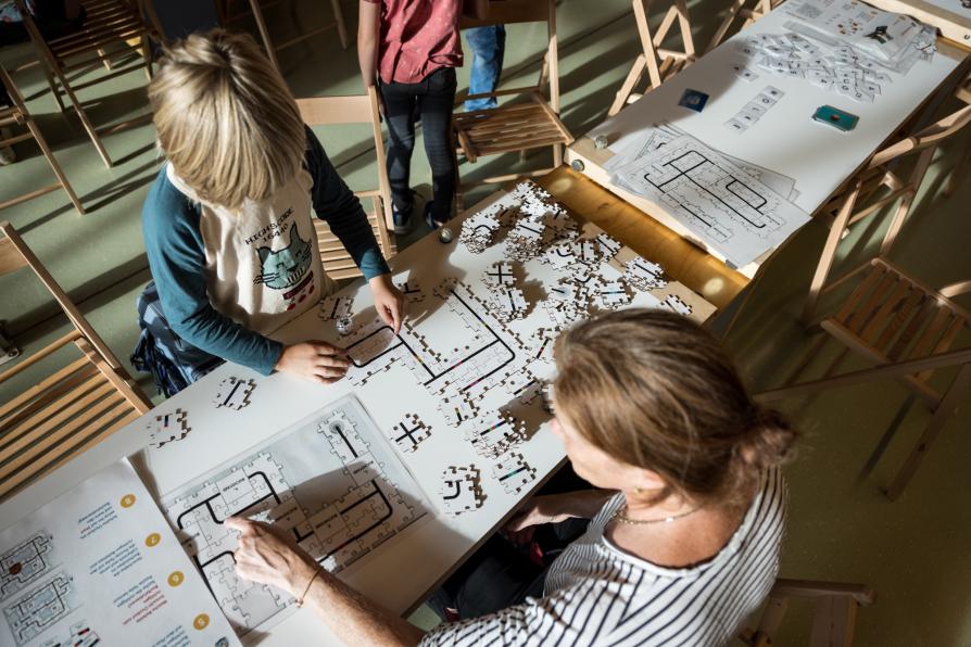 Ein Kind und eine Frau legen aus Puzzleteilen eine Strecke für Roboter.