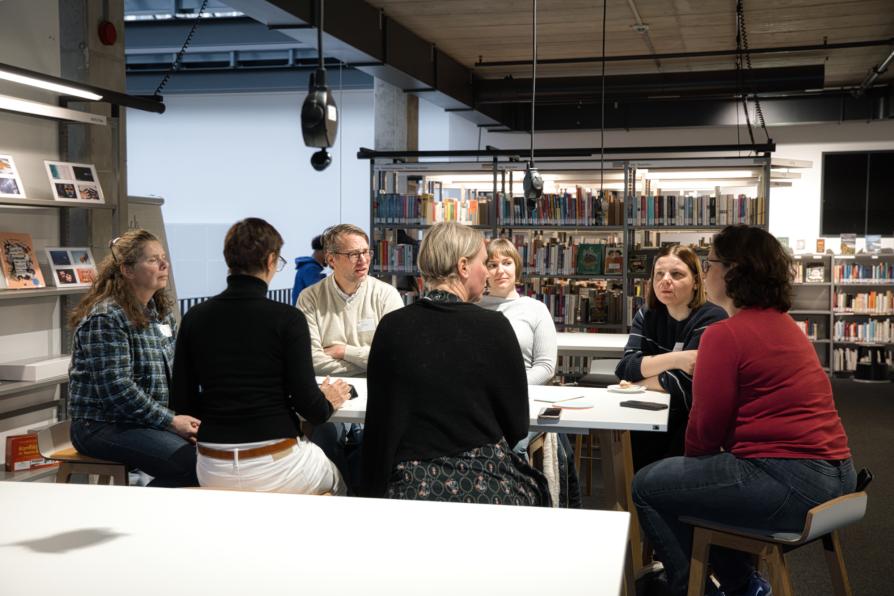 Sieben Personen sitzen um einen Tisch in der Bibliothek.