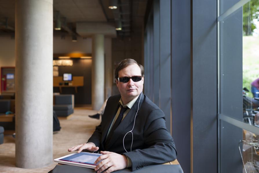 Ein Mann mit einer dunklen Brille sitzt in einer Bibliothek.