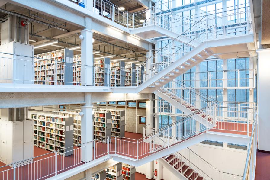 Blick in die Campusbibliothek der Freien Universität Berlin mit Bücherregalen und freier Treppe.