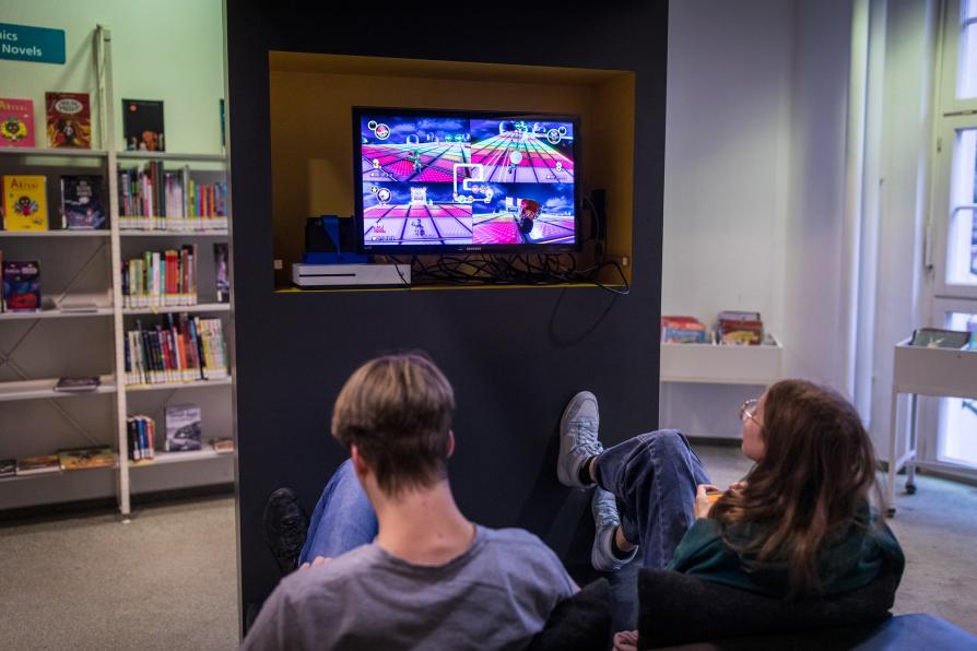 Zwei Personen spielen in der Bibliothek ein Videogame.